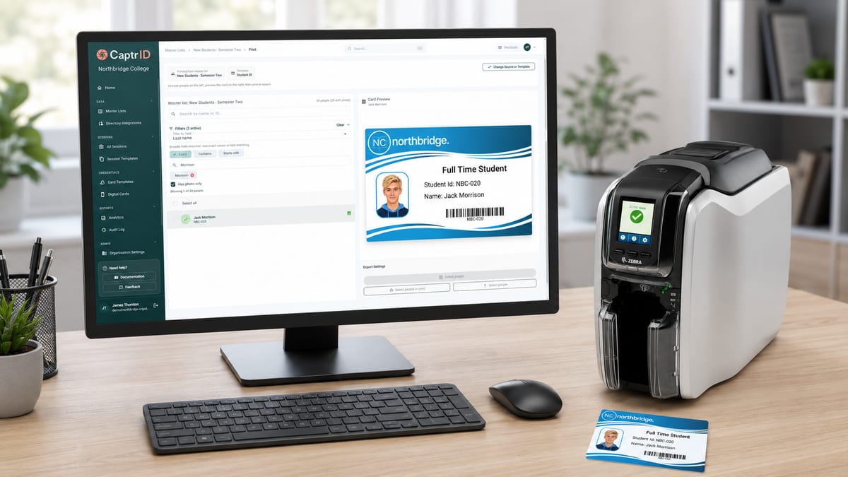 A CaptrID card design on a monitor beside a card printer, with a freshly printed ID card on the desk